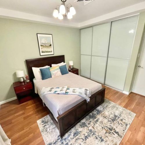 Bedroom with queen bed, decorative pillows, sliding wardrobe doors and wood flooring