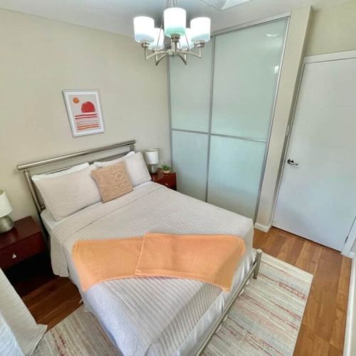 Bedroom with queen bed, soft beige bedding, orange throw, sliding frosted-glass closet doors, bedside tables with lamps and wall art