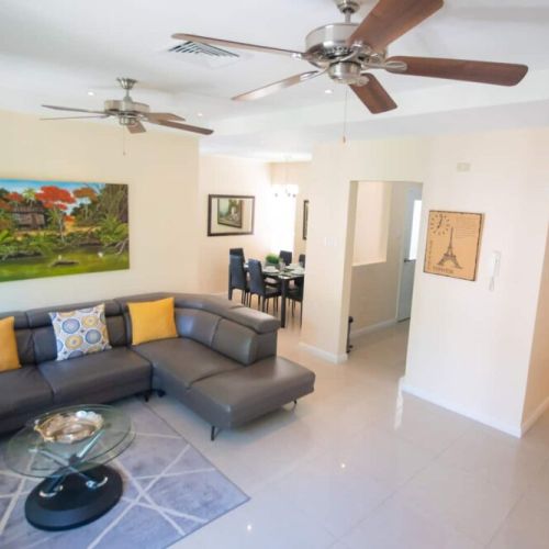 Spacious living room with L-shaped sectional sofa, glass coffee table, colorful cushions and wall art adjacent to dining area
