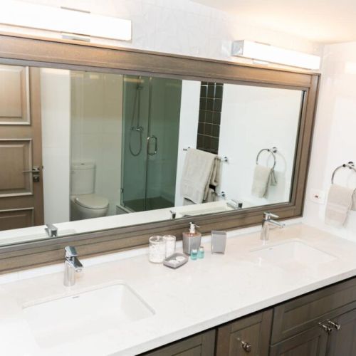 Bathroom with dual vanity sinks, large framed mirror and walk-in shower with glass door