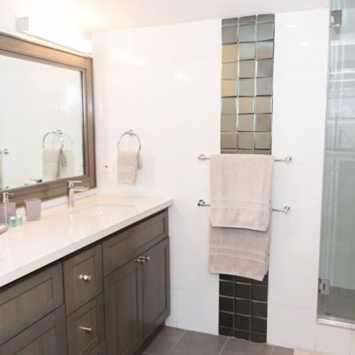 Bathroom with brown vanity and white countertop, large mirror and glass-enclosed shower with mosaic accent tiles