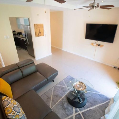 Alternate view of the open-concept living area featuring plush sectional seating, wall-mounted TV, stylish rug and doorway to the kitchen.