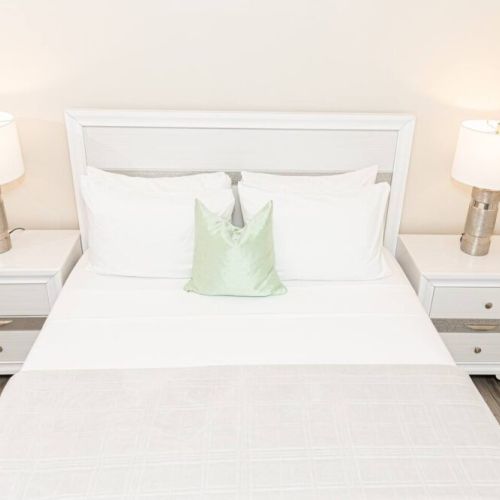 Symmetrical bedroom setup with queen bed, matching white bedside tables and lamps, and green accent pillow