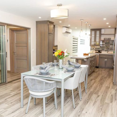 Dining area set for six with modern table and chairs, opening to fully equipped kitchen through wide doorway and glass doors
