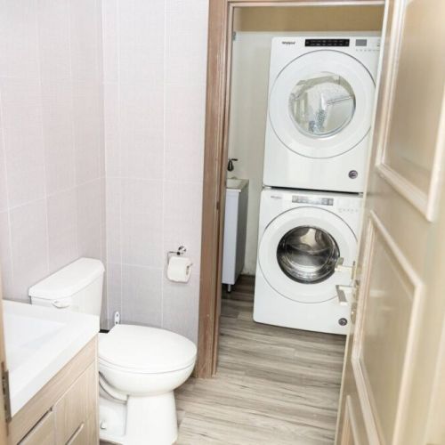 Compact bathroom with toilet and vanity sink adjacent to convenient stacked washer and dryer