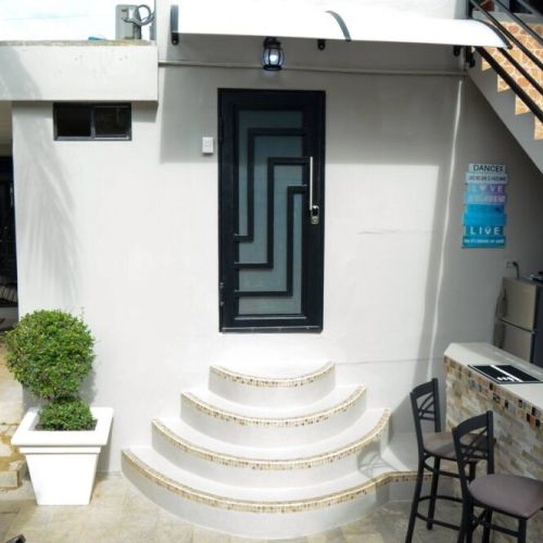 Private apartment entrance featuring a modern black door with geometric design, curved stone steps, canopy, and an adjacent outdoor bar area beneath the staircase.