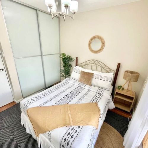 Cozy bedroom with queen bed featuring boho patterned bedding, sliding closet doors, bedside table with lamp and large window