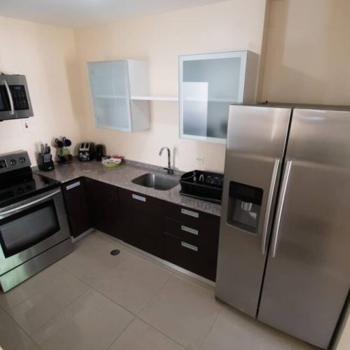 Modern kitchen with stainless-steel appliances, including double-door refrigerator, electric range, microwave, granite countertops and dark cabinetry.