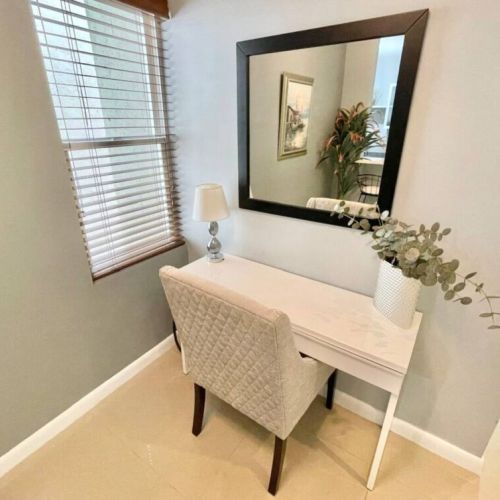 Cozy workspace with writing desk, upholstered chair, table lamp and mirror