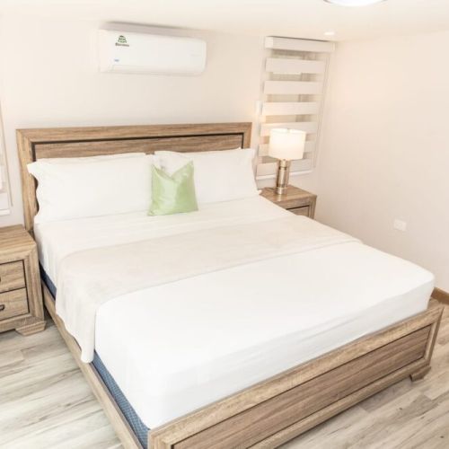 Angle view of bedroom with queen bed, wooden headboard, bedside tables and green accent pillow