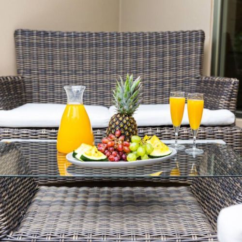 Outdoor wicker seating area with glass-top table featuring fresh fruit platter and carafe of orange juice for relaxing al fresco dining