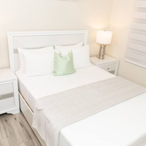 Bright bedroom with queen bed, white headboard, bedside tables with lamps and green accent pillow