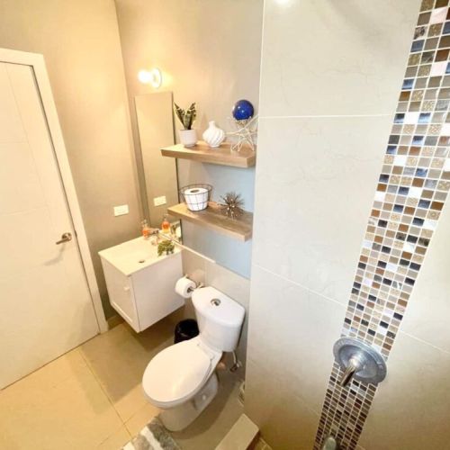 Compact bathroom with glass mosaic accent, floating vanity sink, wall shelf and toilet