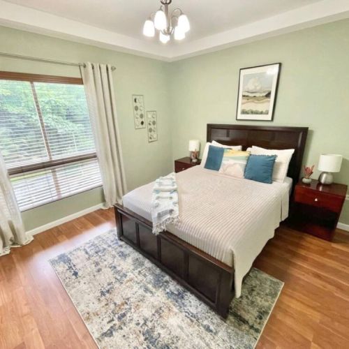 Comfortable bedroom with queen bed, plush pillows, wooden headboard, bedside tables with lamps, and large window