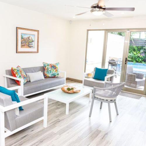 Bright living room with modern seating, colourful cushions and sliding glass doors overlooking the pool