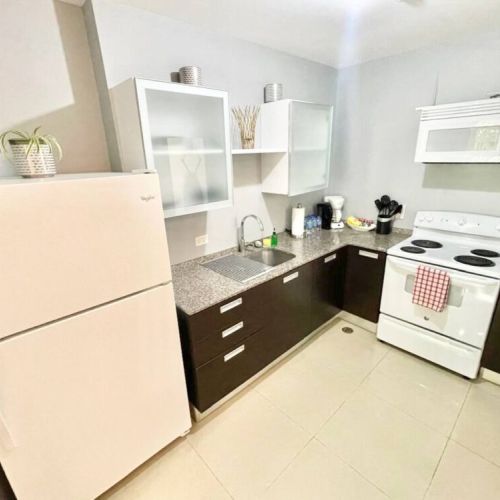 Fully equipped kitchen with white refrigerator, stove, microwave, dark cabinets and granite countertops