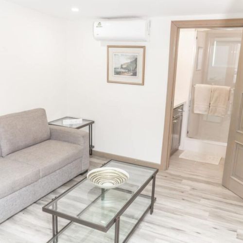 Cozy living area with grey sofa and glass coffee table, adjacent to bathroom with glass-enclosed shower