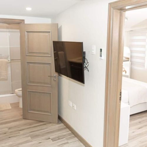 Hallway with wall-mounted TV leading to bedroom and bathroom with glass-enclosed shower
