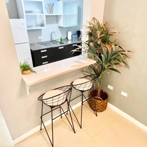 Breakfast bar with two bar stools, white countertop, and decorative potted plants overlooking kitchen